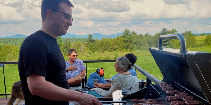 Eternity Founder, Mike Lannen manning the grill at an Eternity Team BBQ while team members chat in the background